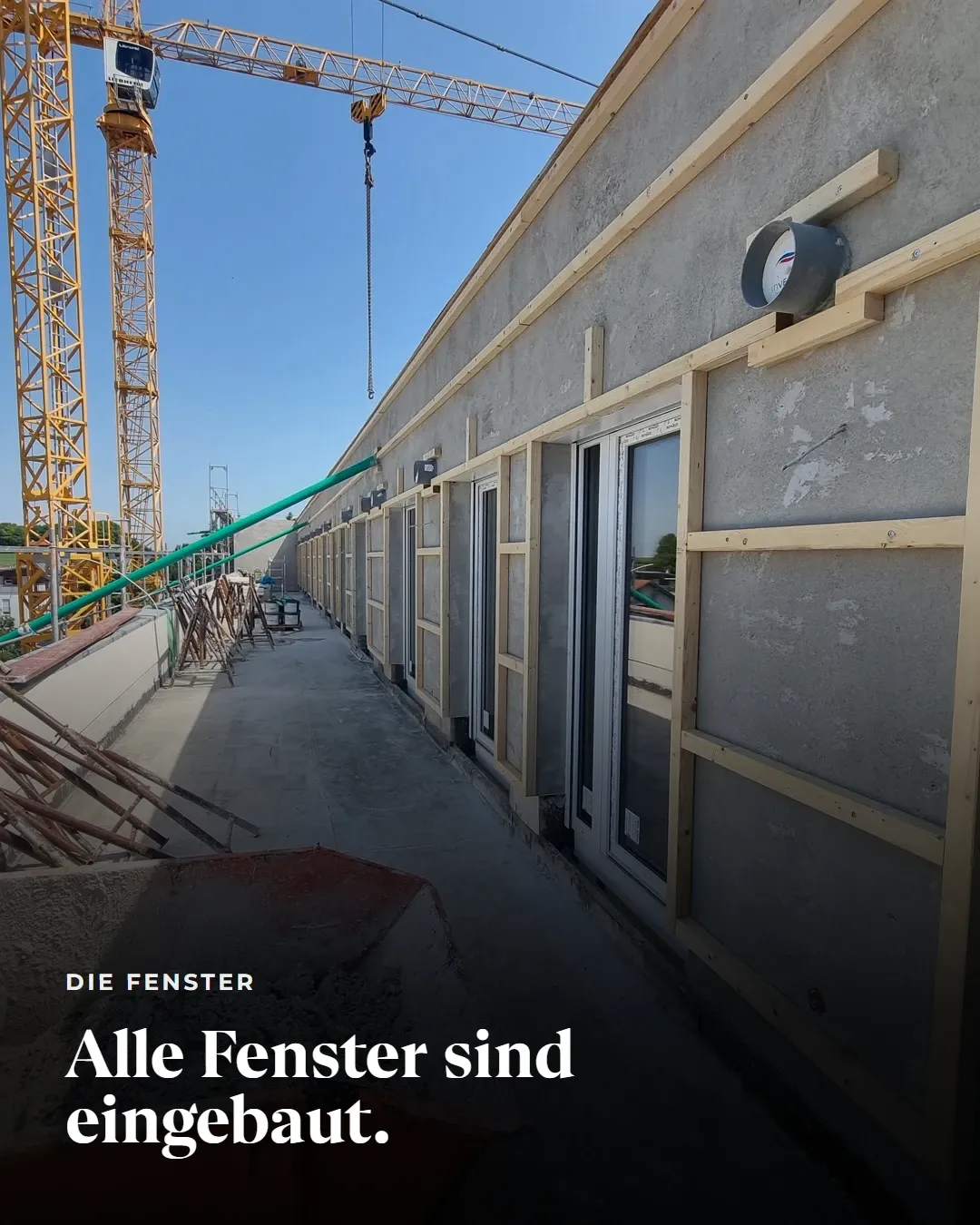 Die Fenster: Alle Fenster sind eingebaut. Blick entlang einer Terrasse mit eingebauten Fenstertüren, im Hintergrund zwei Baukräne.