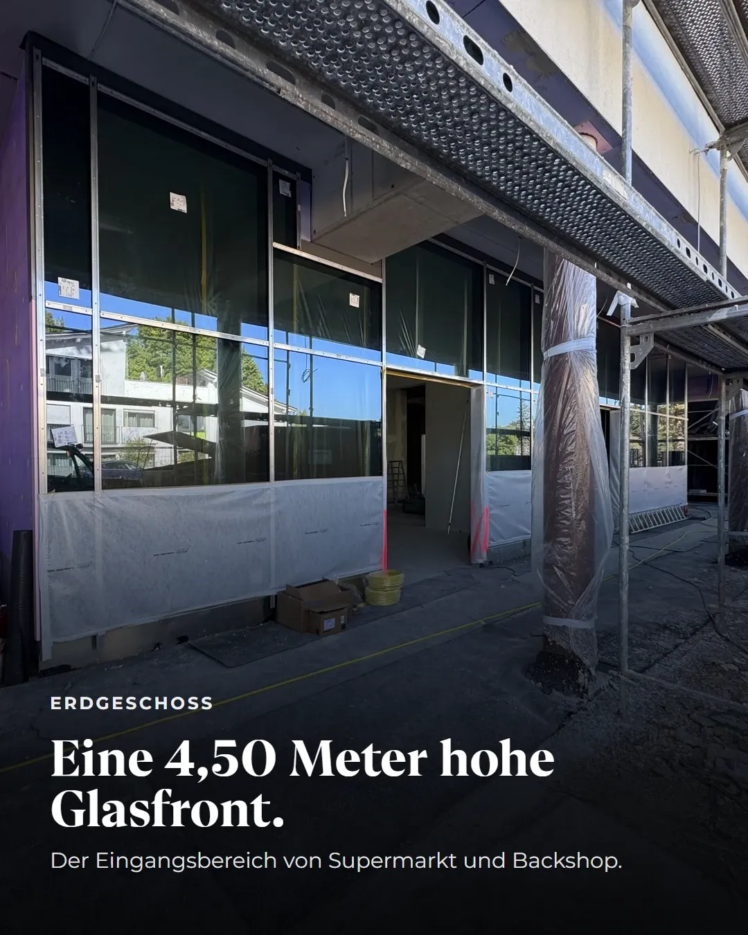 Erdgeschoss: Eine 4,50 Meter hohe Glasfront. Der Eingangsbereich von Supermarkt und Backshop. Blick auf die eingebaute, noch mit Folie geschützte Glasfassade.