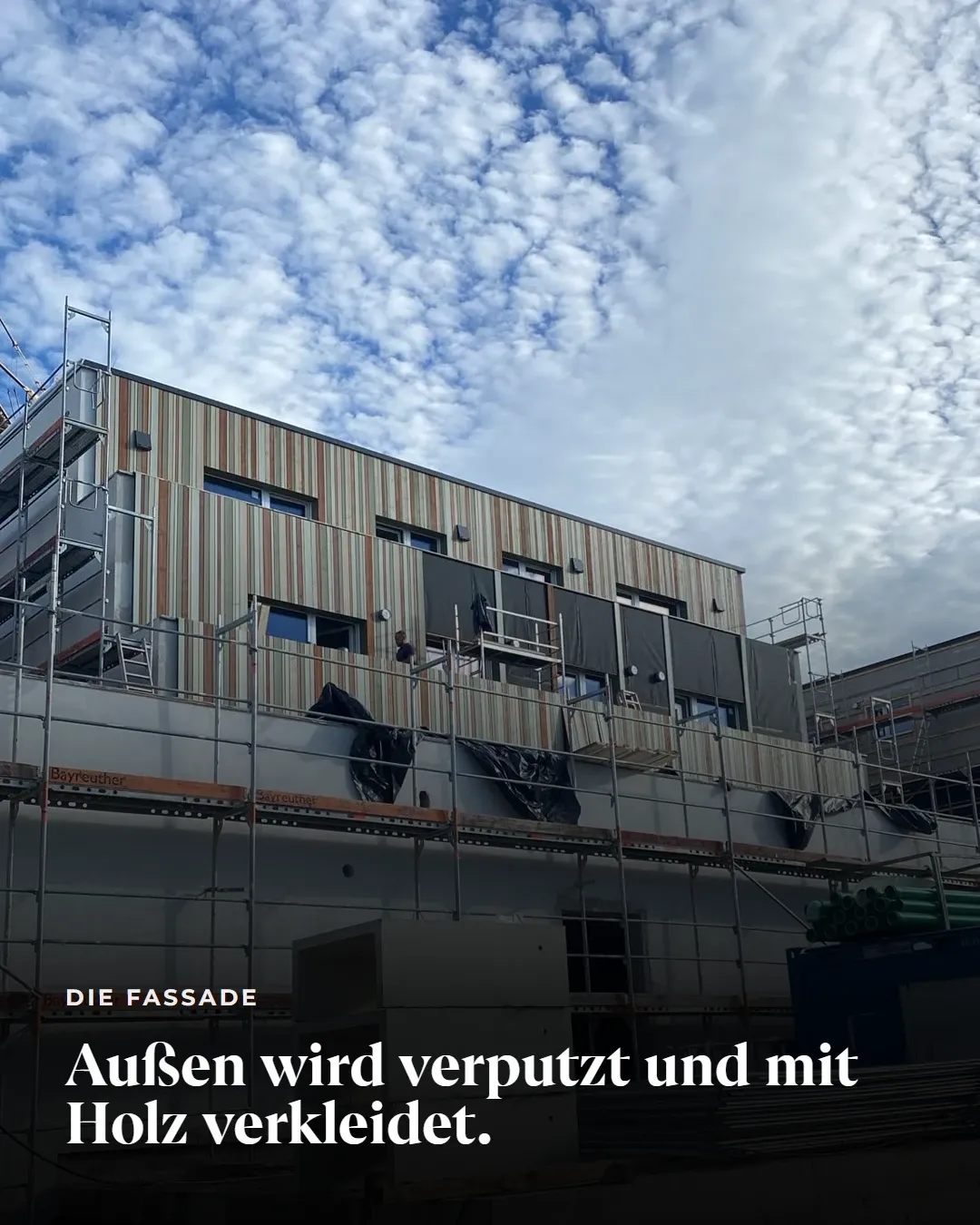 Die Fassade: Außen wird verputzt und mit Holz verkleidet. Blick auf die teilweise mit Holz verkleidete Fassade, davor das Gerüst.